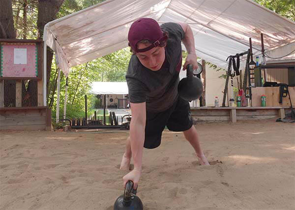 An image of a youth athlete training in a sand pit doing kettlebell rows